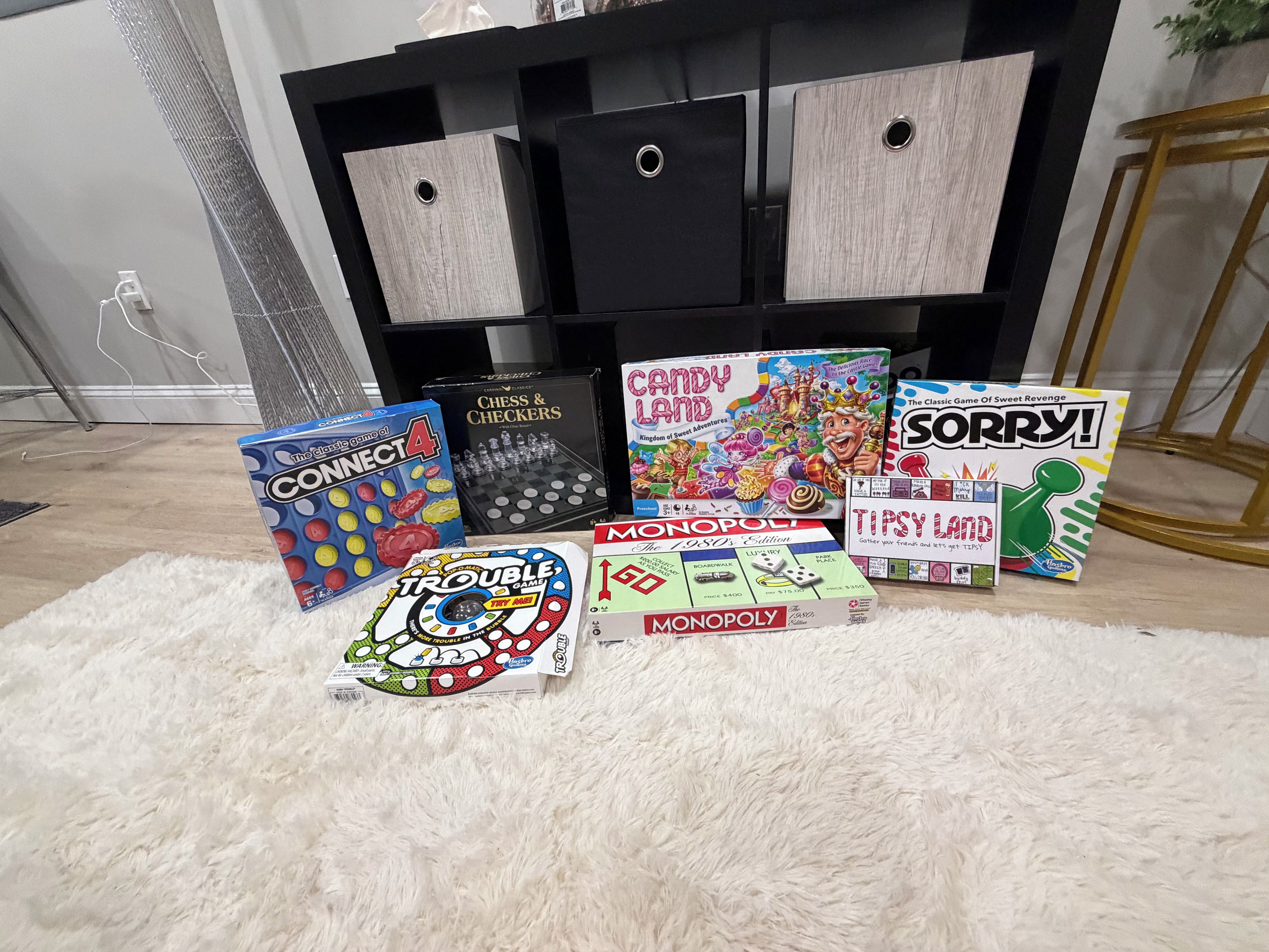 Een verzameling gezelschapsspellen op een witte vloerkleed voor een zwarte entertainmentskast.