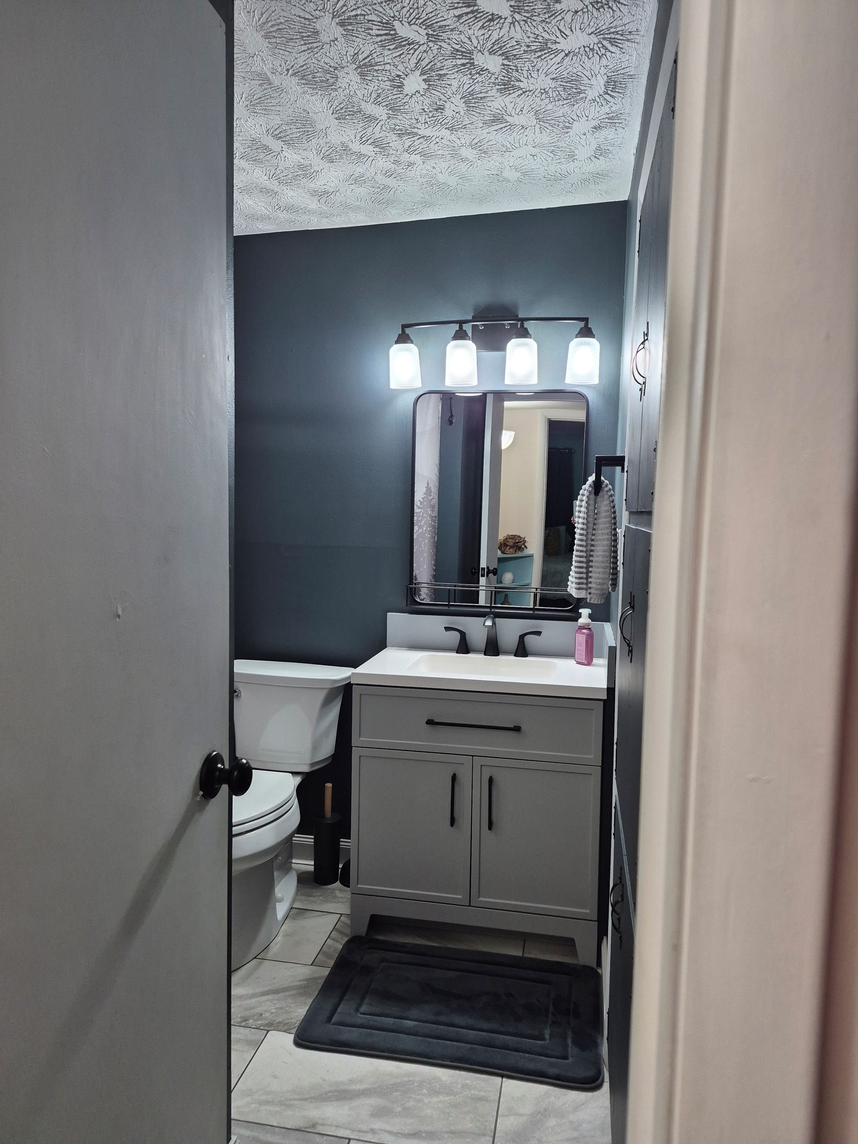A bathroom with a toilet, sink, mirror, and a light fixture above the mirror.