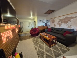 A living room with a brick wall, a wooden coffee table, a red bean bag chair, a grey sofa with red cushions, and a world map on the wall.