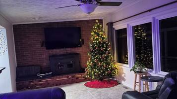 A living room with a fireplace, a Christmas tree, a ceiling fan, and a large window.