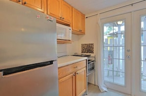 A kitchen with wooden cabinets, a white refrigerator, a microwave, and a stove. - Charming Beach Cottage Steps from Village (Siesta Key)