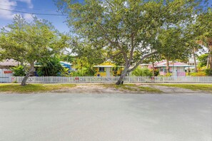 A residential street with houses, a white picket fence, and a clear sky. - Charming Beach Cottage Steps from Village (Siesta Key)