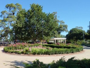Un jardin aménagé avec un arbre central, un belvédère blanc et un chemin pavé.