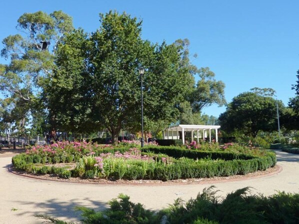 Un giardino curato con un albero centrale, un gazebo bianco e un vialetto lastricato.