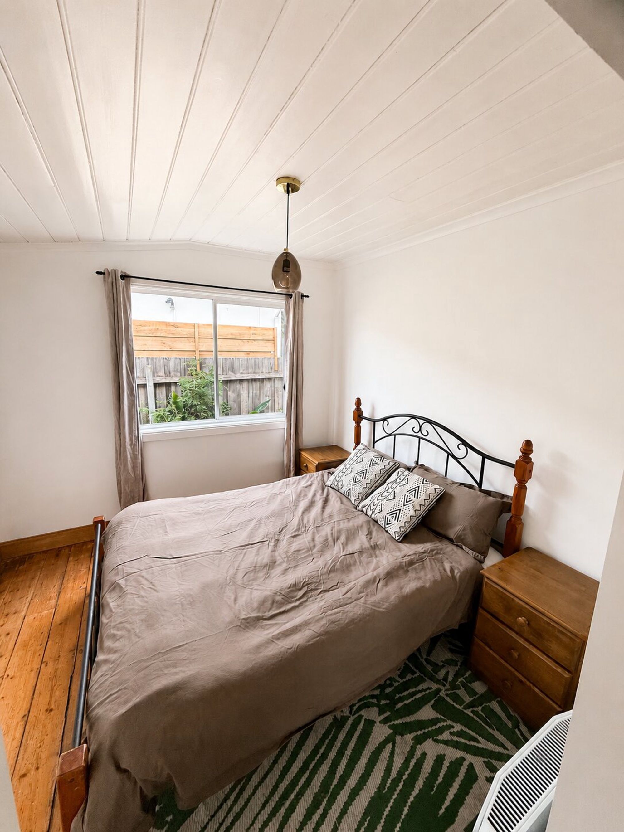 A bedroom with a bed, a nightstand, a window with curtains, and a ceiling fan.