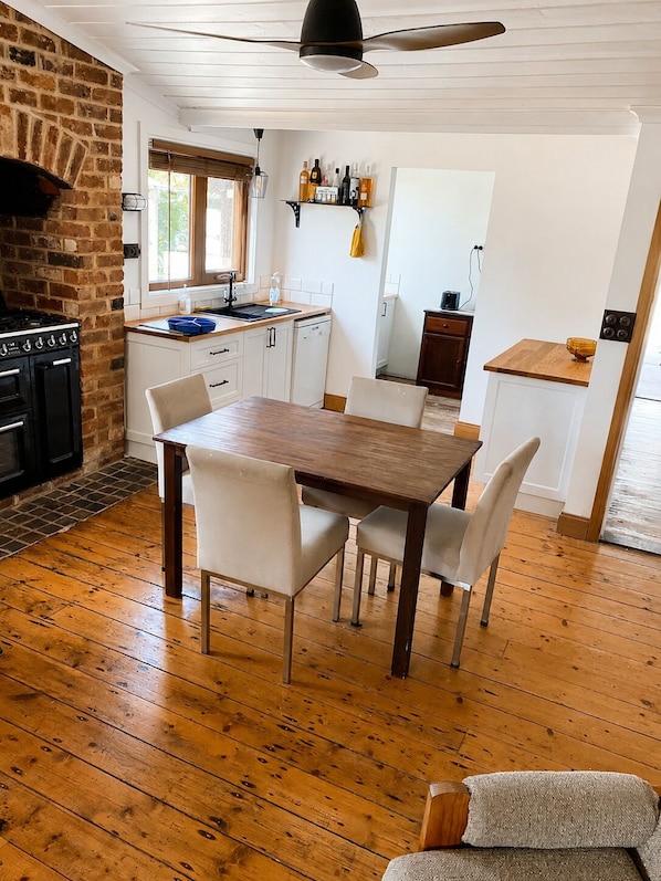 A kitchen with a brick wall, wooden floor, and a dining area with a table and chairs.