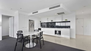 A modern kitchen with white cabinetry, a central island, and a dining area with a round table and chairs. - Circle On Cavil Apartment 2146 (Surfers Paradise)