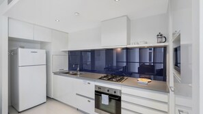 A modern kitchen with white cabinetry, a built-in stove, and a large window overlooking a dining area. - Circle On Cavil Apartment 2205 (Surfers Paradise)