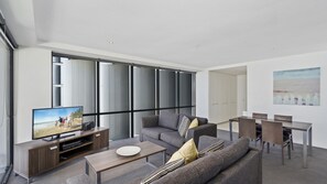 A modern living room with a sofa, coffee table, TV, and a dining area with chairs and a table. - Circle On Cavil Apartment 2205 (Surfers Paradise)