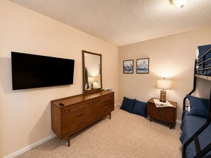Ein Schlafzimmer mit Fernseher, Schminktisch, Etagenbett und zwei Bildern.
