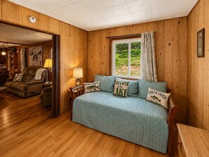 Ein gemütliches Zimmer mit einem Bett, einem Fenster mit Vorhängen, einer Lampe und einer Holzwand.