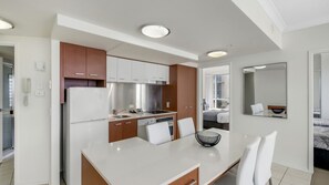 A modern kitchen with white cabinets, stainless steel appliances, and a dining area with a white table and chairs. - Chevron Renaissance Apartment 1092 (Surfers Paradise)