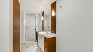 A modern bathroom with a glass shower enclosure, a white sink, and wooden cabinetry. - Chevron Renaissance Apartment 1092 (Surfers Paradise)