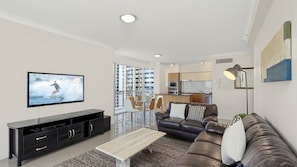 A modern living room with a flat-screen TV, a leather sofa, a coffee table, and a dining area with chairs. - Chevron Renaissance Apartment 1135 (Surfers Paradise)
