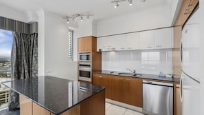 A modern kitchen with a central island, stainless steel appliances, and wooden cabinets. - Chevron Renaissance Apartment 1224 (Surfers Paradise)