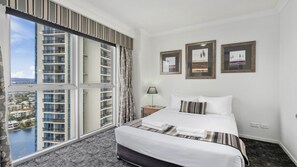 A hotel room with a large window, a bed, a nightstand, and three framed pictures on the wall. - Chevron Renaissance Apartment 1224 (Surfers Paradise)