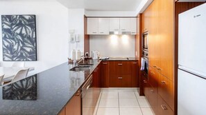 A modern kitchen with wooden cabinets, a black countertop, and a stainless steel refrigerator. - Chevron Renaissance Apartment 1262 (Surfers Paradise)