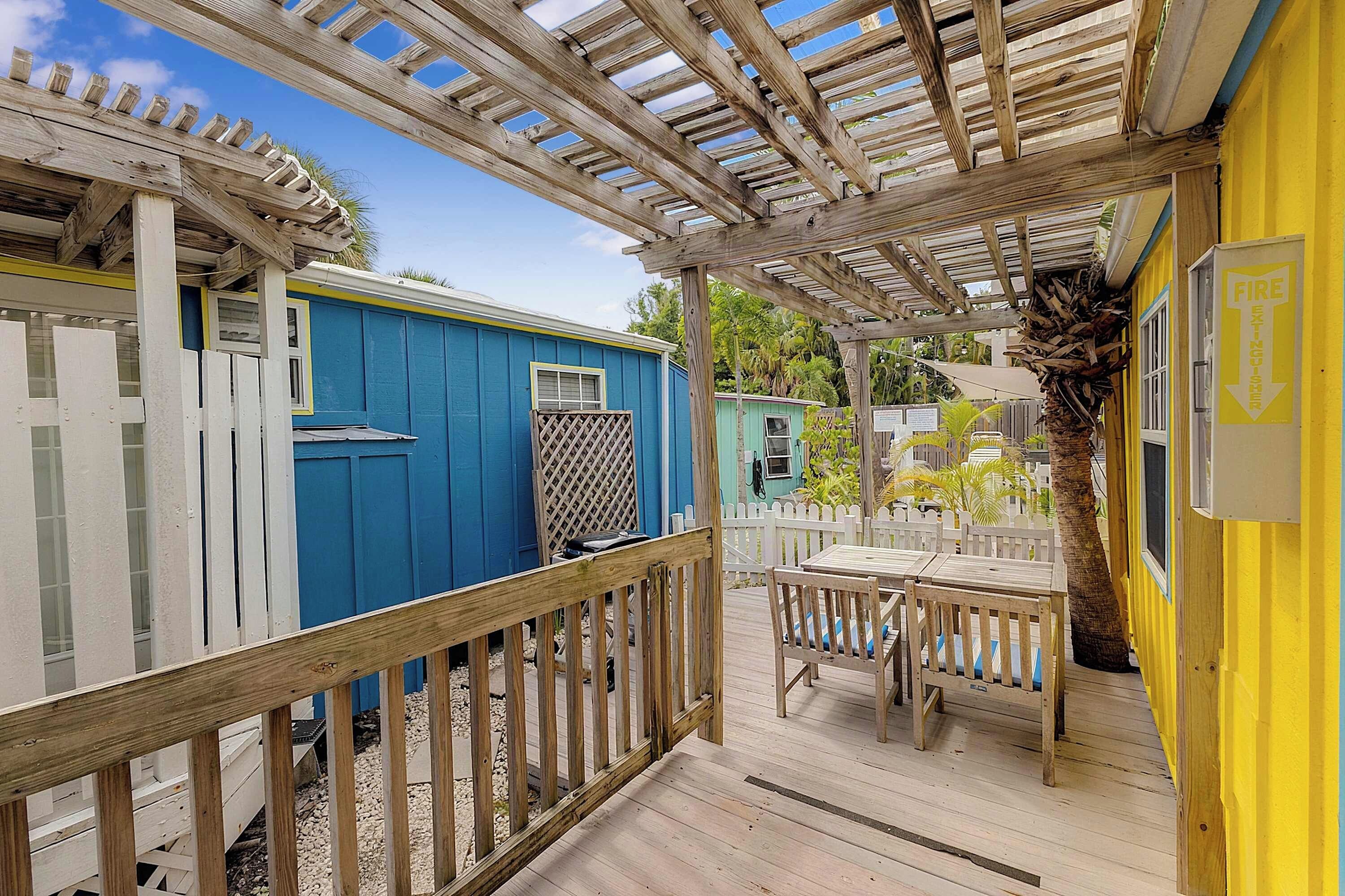 Katettu ulkoalue, jossa on puinen terassi, valkoinen puinen aita ja keltainen rakennus, jonka seinässä on palosammuttimen merkki.