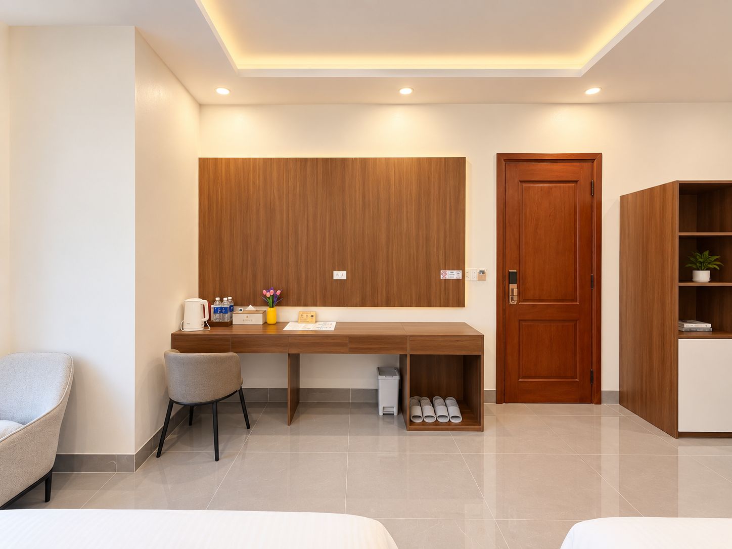 A modern hotel room with a wooden desk, two chairs, a small trash bin, and a wardrobe.
