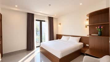 Quarto de hotel moderno com uma cama grande, cabeceira de madeira, mesa de cabeceira, área de estar e vista pela janela.