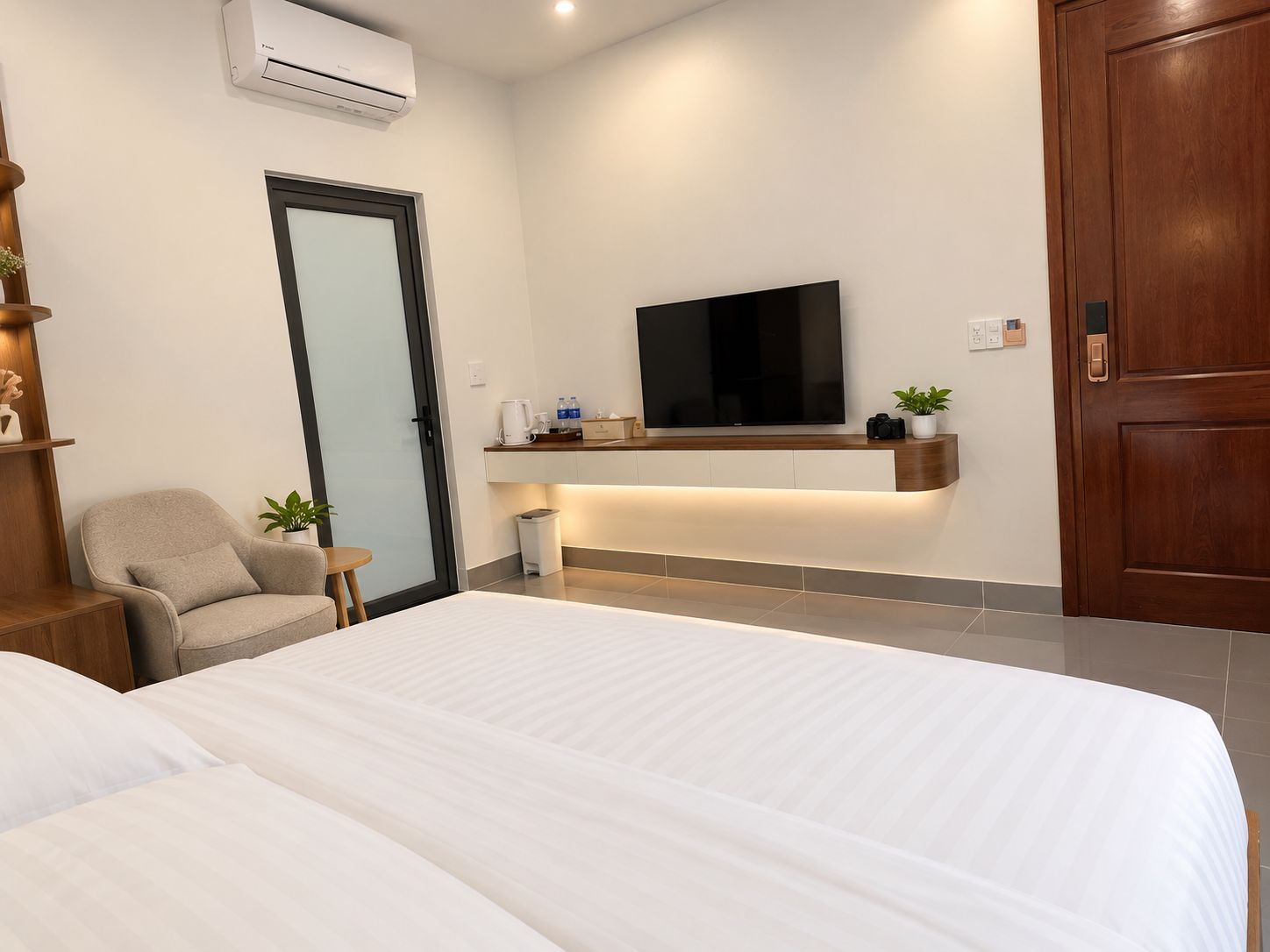 Una habitación de hotel moderna con una cama grande, un televisor montado en la pared, una pequeña zona de estar y una puerta de madera.