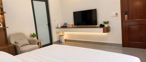 Una habitación de hotel moderna con una cama grande, un televisor montado en la pared, una pequeña zona de estar y una puerta de madera.