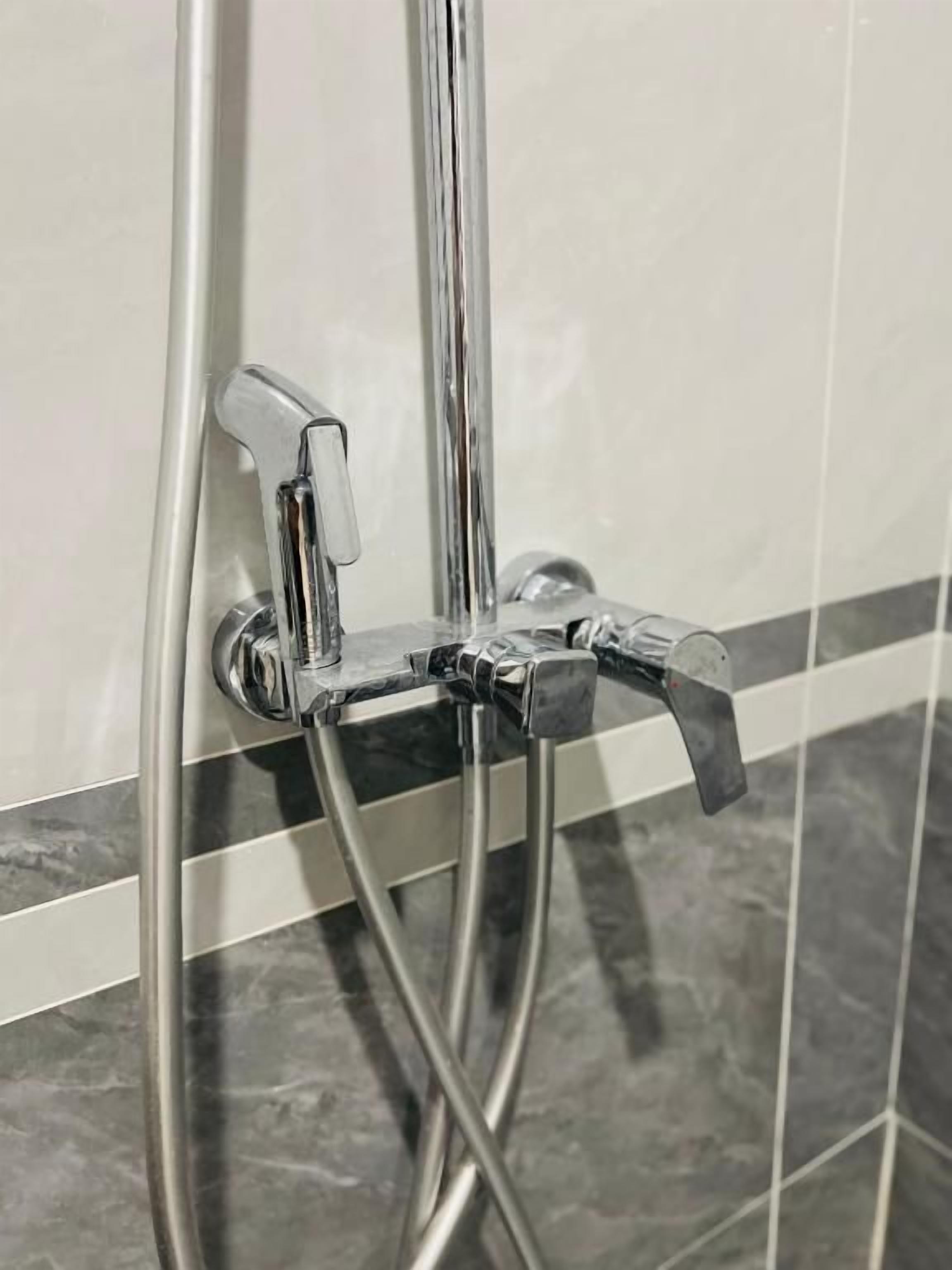 Una ducha con grifería cromada y pared de azulejos.