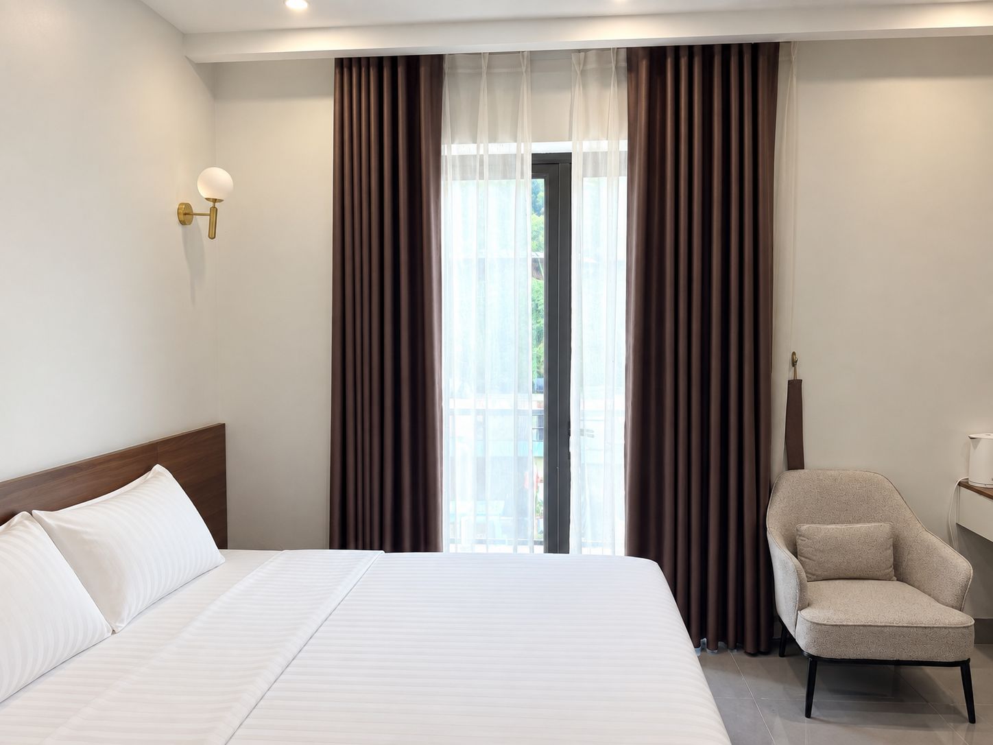 Una camera d'albergo con un letto grande, una sedia, un comodino e una finestra con tende.