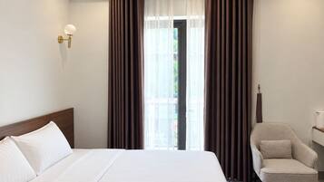 Una camera d'albergo con un letto grande, una sedia, un comodino e una finestra con tende.
