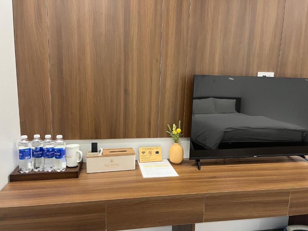 Habitación de hotel con cabecera de madera, televisor de pantalla plana, escritorio de madera con bandeja que contiene botellas de agua, taza de café, caja de té y un pequeño jarrón con flores.