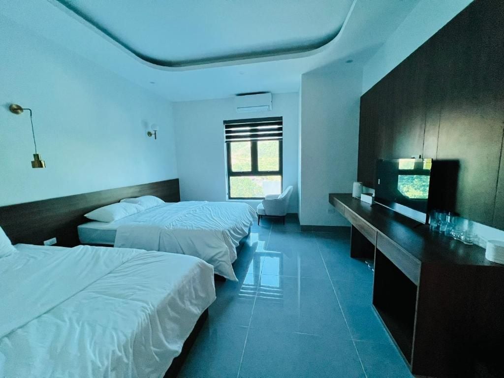 A hotel room with two beds, a desk, a chair, a TV, and a window with blinds.