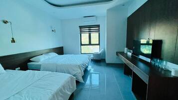 A hotel room with two beds, a desk, a chair, a TV, and a window with blinds.