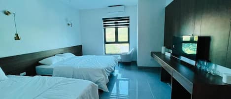 A hotel room with two beds, a desk, a chair, a TV, and a window with blinds.