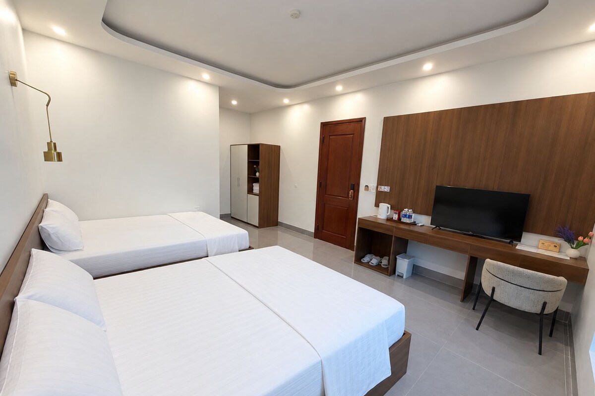 Una habitación de hotel con dos camas individuales, un armario de madera, un escritorio con televisor y una silla.