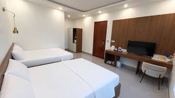 A hotel room with two single beds, a wooden wardrobe, a desk with a television, and a chair.