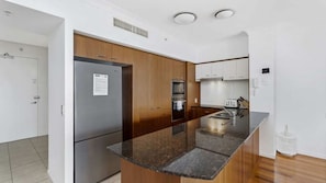 A modern kitchen with stainless steel appliances, wooden cabinets, and a granite countertop. - Chevron Renaissance Apartment 1323 (Surfers Paradise)