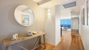 A modern interior with a wooden console table, a round mirror, and a view of a balcony with outdoor furniture. - Chevron Renaissance Apartment 1333 (Surfers Paradise)