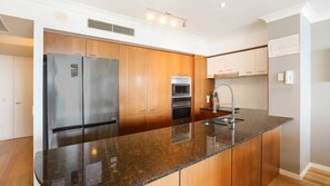 A modern kitchen with stainless steel appliances, wooden cabinets, and a granite countertop. - Chevron Renaissance Apartment 1333 (Surfers Paradise)