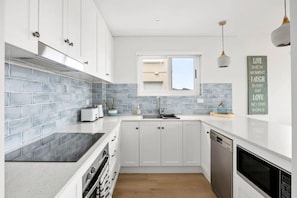 A modern kitchen with white cabinets, grey tiled backsplash, and stainless steel appliances. - Beautiful Apartment | Manly Beach Views & Parking (Queenscliff)