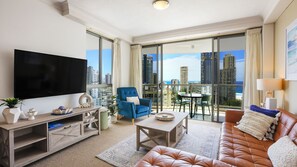 A modern living room with a flat-screen TV, a blue armchair, a leather sofa, and a balcony with a city view. - Chevron Renaissance Apartment 2172 (Surfers Paradise)