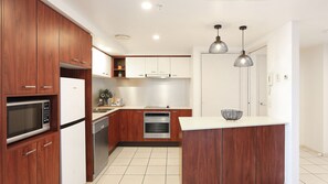 A modern kitchen with wooden cabinets, stainless steel appliances, and pendant lighting. - Chevron Renaissance Apartment 2172 (Surfers Paradise)