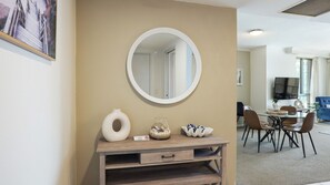 A room with a round mirror, a wooden console table with decorative items, and a dining area with chairs and a table. - Chevron Renaissance Apartment 2172 (Surfers Paradise)
