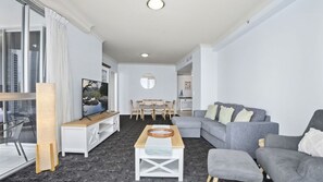 Ein modernes Wohnzimmer mit einer Eckcouch, einem Couchtisch, einem Fernseher und einem Essbereich mit Stühlen und einem Tisch.