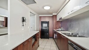 Eine moderne Küche mit weißen Arbeitsplatten, Holzschränken, einem schwarzen Kühlschrank und Edelstahlgeräten.