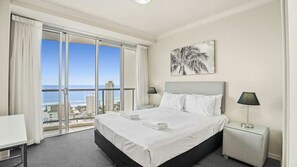 A hotel room with a large bed, two bedside tables, a view of the ocean, and a palm tree painting on the wall. - Chevron Renaissance Apartment 2215 (Surfers Paradise)