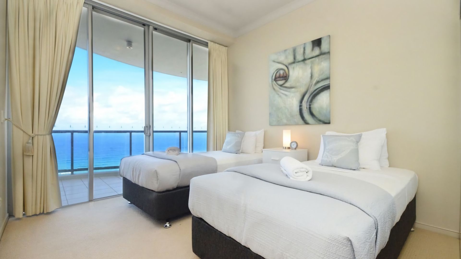 A hotel room with two beds, a large window with a view of the sea, and a painting on the wall.