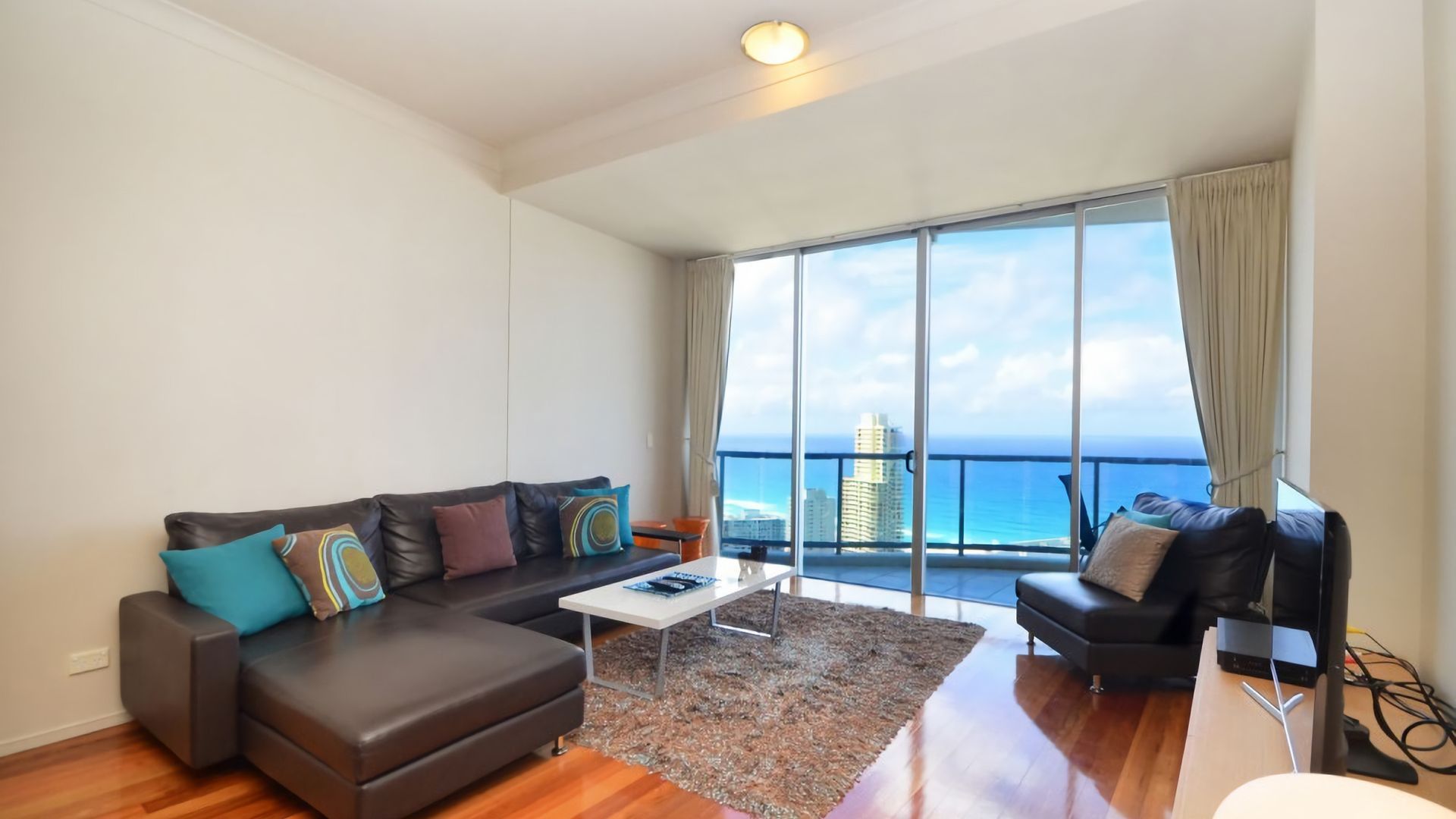 A spacious living room with a large window offering a view of the ocean and city skyline.