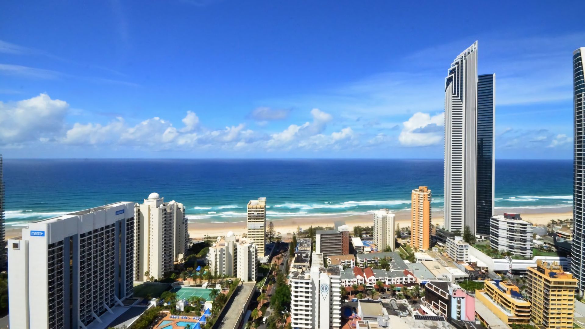 Eine Küstenstadt mit hoch aufragenden Gebäuden, einem Strand und blauem Himmel.