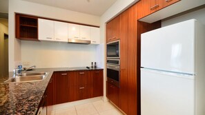 A modern kitchen with granite countertops, stainless steel appliances, and wooden cabinetry. - Chevron Renaissance Apartment 2364 (Surfers Paradise)