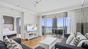 A modern hotel room with a balcony, a bed, a TV, and a seating area with a view of the city and ocean. - Chevron Renaissance Apartment 2402 (Surfers Paradise)